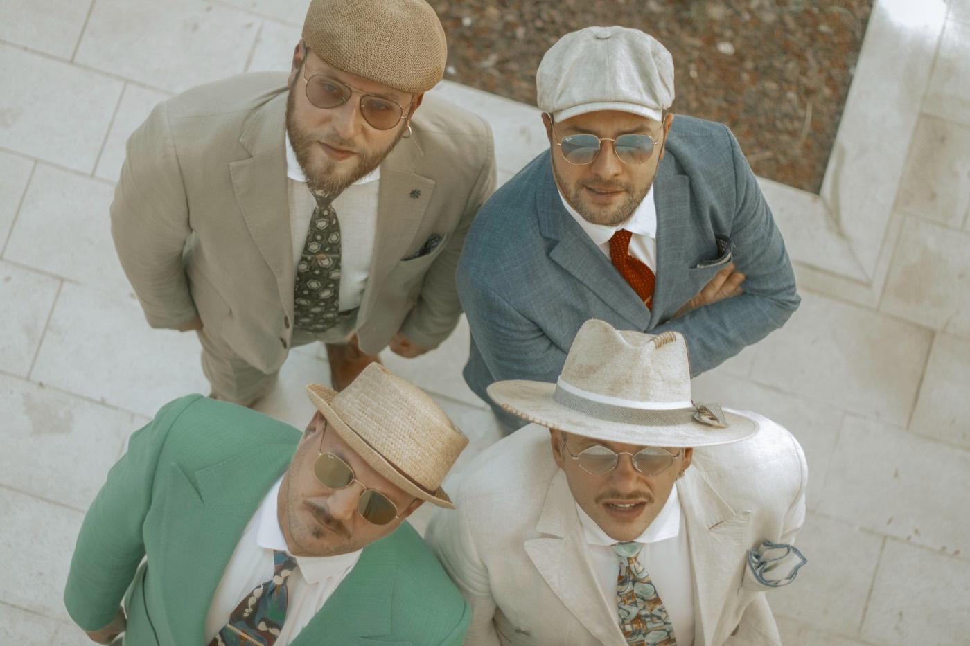 I quattro musicisti della Dr. Jazz & Dirty Bucks Swing Band ripresi dall'alto, in abiti di lino chiari e cappelli di paglia